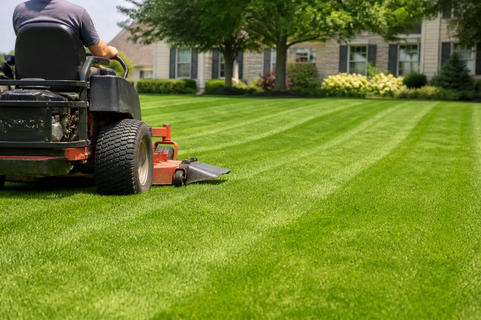 Professional riding mower cutting a freshly striped green lawn